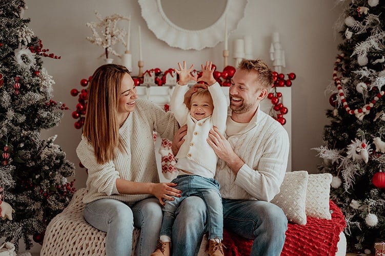Parents laughing with their child between decorated Christmas trees