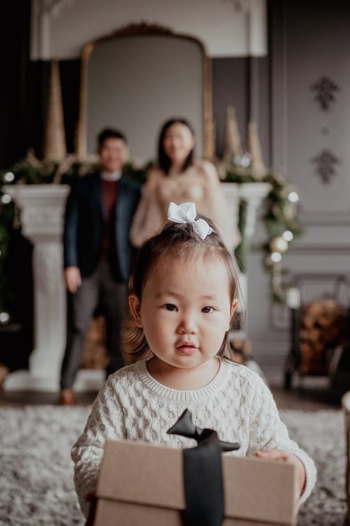 Child holding a wrapped gift with parents beside a decorated fireplace